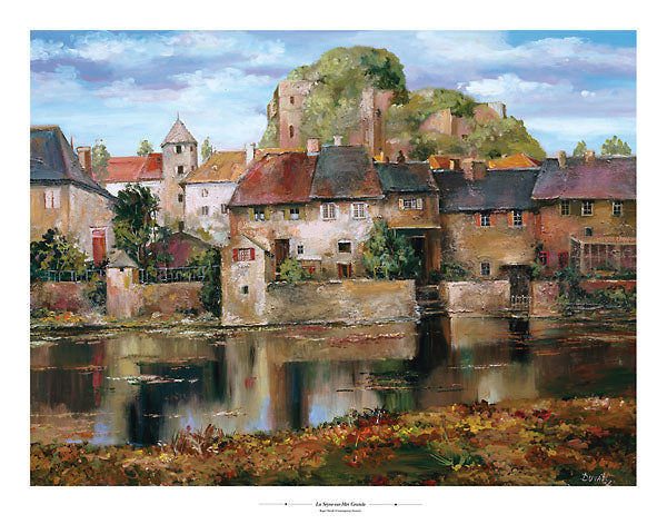 An old town with colourful roofs. A small lake separates the viewer from the town. An overgrown castle is hidden behind the houses.