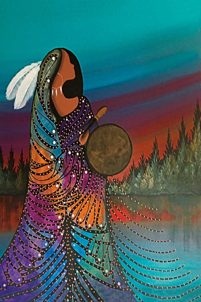 A woman in a colourful gown and white feathers in her hair. She holds a leather drum. She stands at the edge of a lake, trees surrounding it.