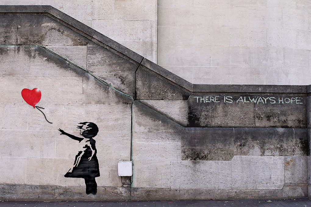 A girl reaches for a red, heart-shaped balloon which floats away from her. Near by text written in chalk reads: "There is Always Hope." Artwork stenciled onto a wall.
