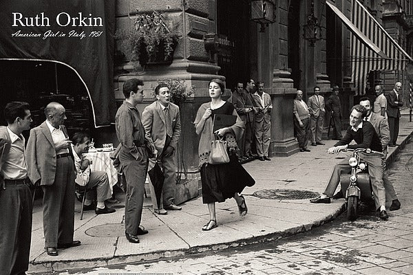 Black and White photo. A young, caucasian woman walks along a sidewalk to a corner. Several men are looking at her. One sits on a moped, smiling at her. Another whistles or is making kissing lips at her. She appears to be in distress.