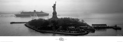 A black and white photo of New York City's Liberty Island. The Statue of Liberty stand atop the island and a boat floats behind it.