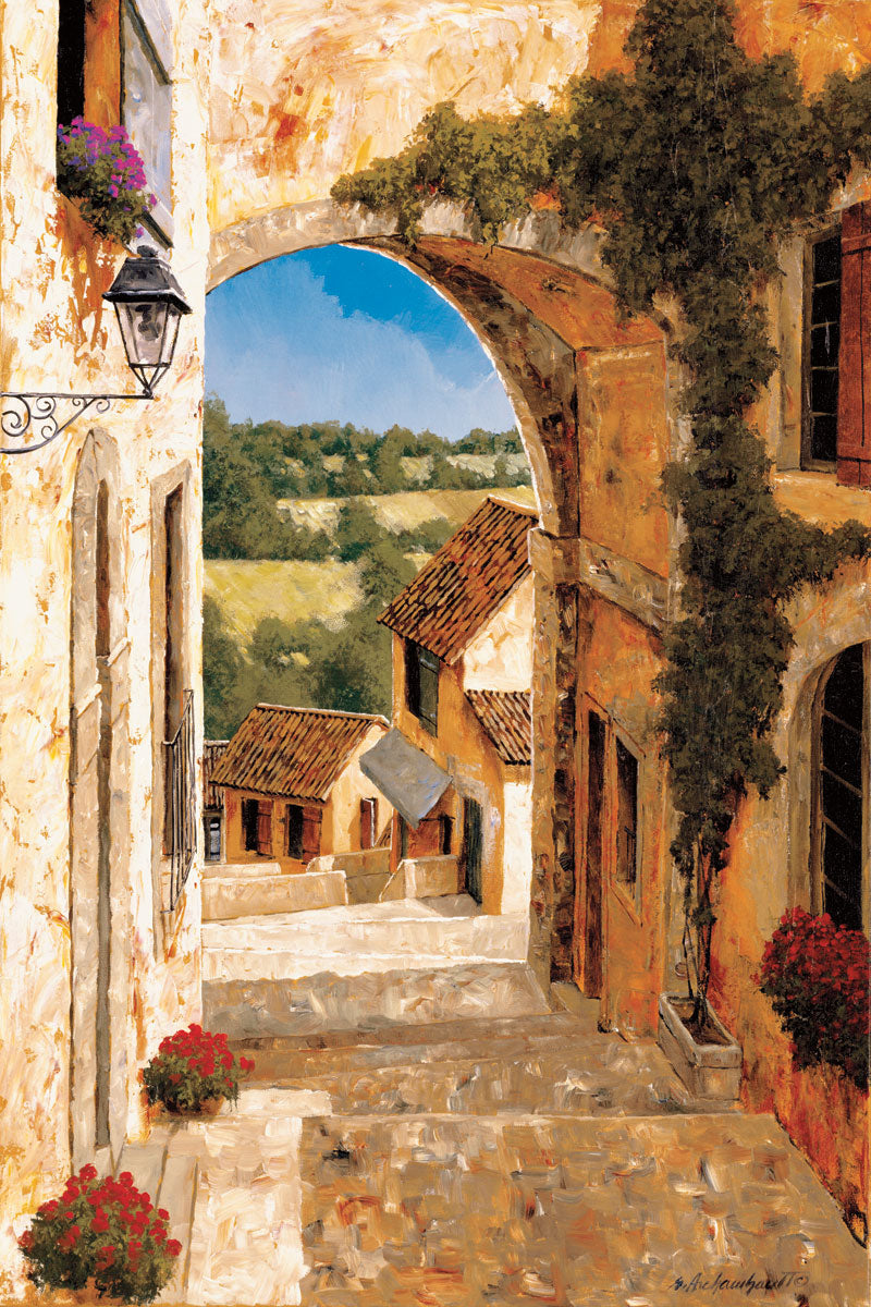 An arch in a rustic village. The countryside can be seen in the distance. Houses stand on the side of the stone road down the hill.