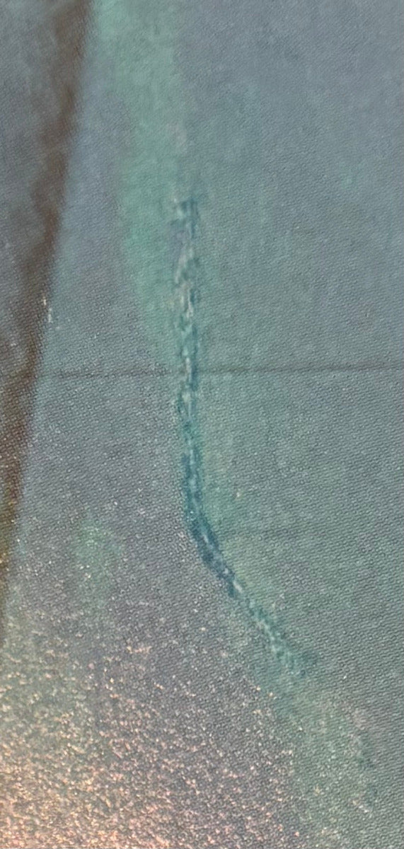 A close-up of a textured, shimmering material surface in a muted teal-green color with a subtle sheen. Show slight damage to paper. 