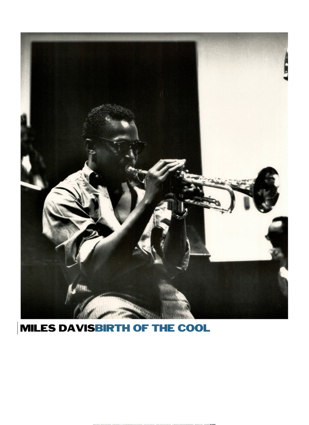 A black and white photo of Miles Davis playing his trumpet in the studio. He wears a pair of sunglasses. 