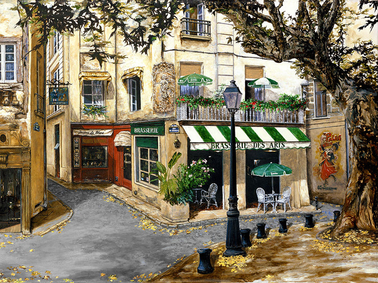 A rustic, French street with a branching road. Storefronts line the street, a restaurant on the corner called "Brasserie des Arts" on its awning. There is a porch above the restaurant with flowers along the railing and two umbrellas. Across the street is a street lamp and a leafless tree, its yellow leaves decorating the sidewalk and road.