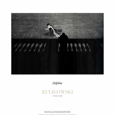 A black and white photo print. A woman in a black dress lays on the ground. A silhouetted man stands at a silhouetted rail, looking down at the woman. 