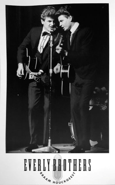 The Everly Brothers playing their acoustic guitars and sining into the mic. They both wear suits. 