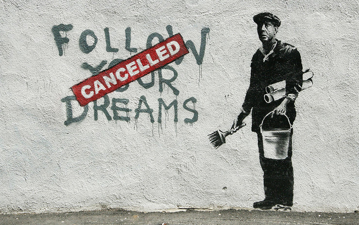 "Follow Your Dreams" is spray painted onto a wall. A red "Cancelled" sign covers the text. A man in a flat cap stands next to the text. He carries a paint brush and a bucket of glue. Artwork stenciled onto the wall.