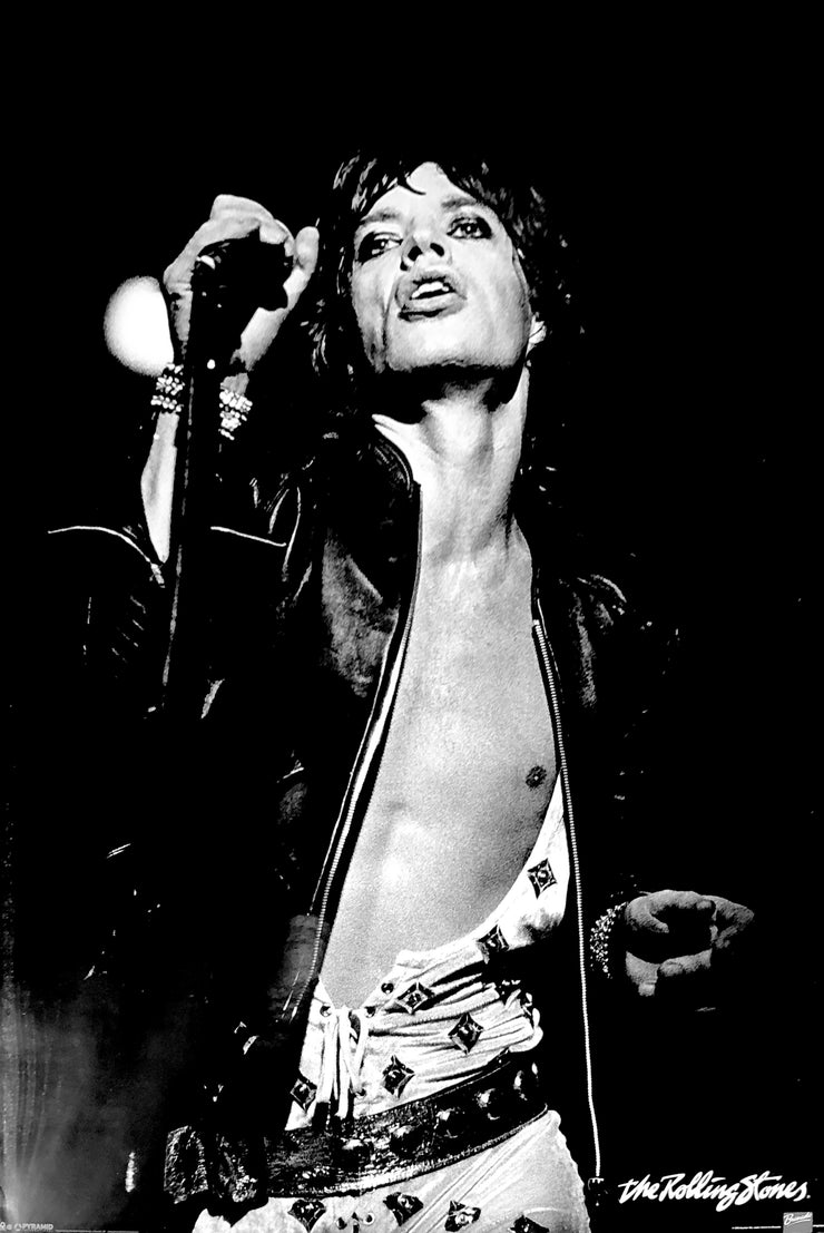 black and white photo of mick jagger singing. He hold the mic in his right hand. His back jacket is open, revealing his bare chest. 