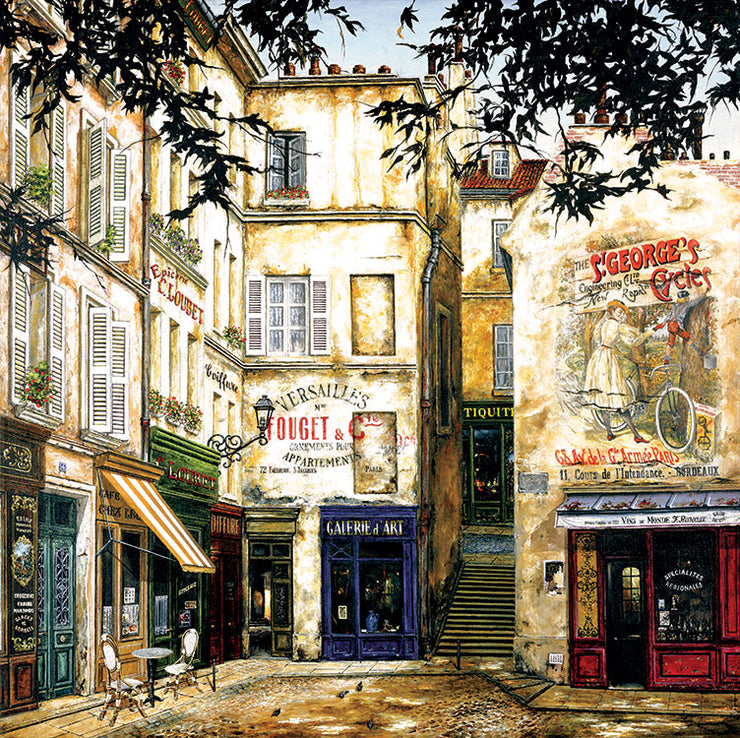 A French street corner, with classic stone buildings. There is a mural above a storefront of a woman with a bicycle. Storefronts are squeezed together along the cobble road, with some chairs and a table out. Stairs lead to an elevated street.