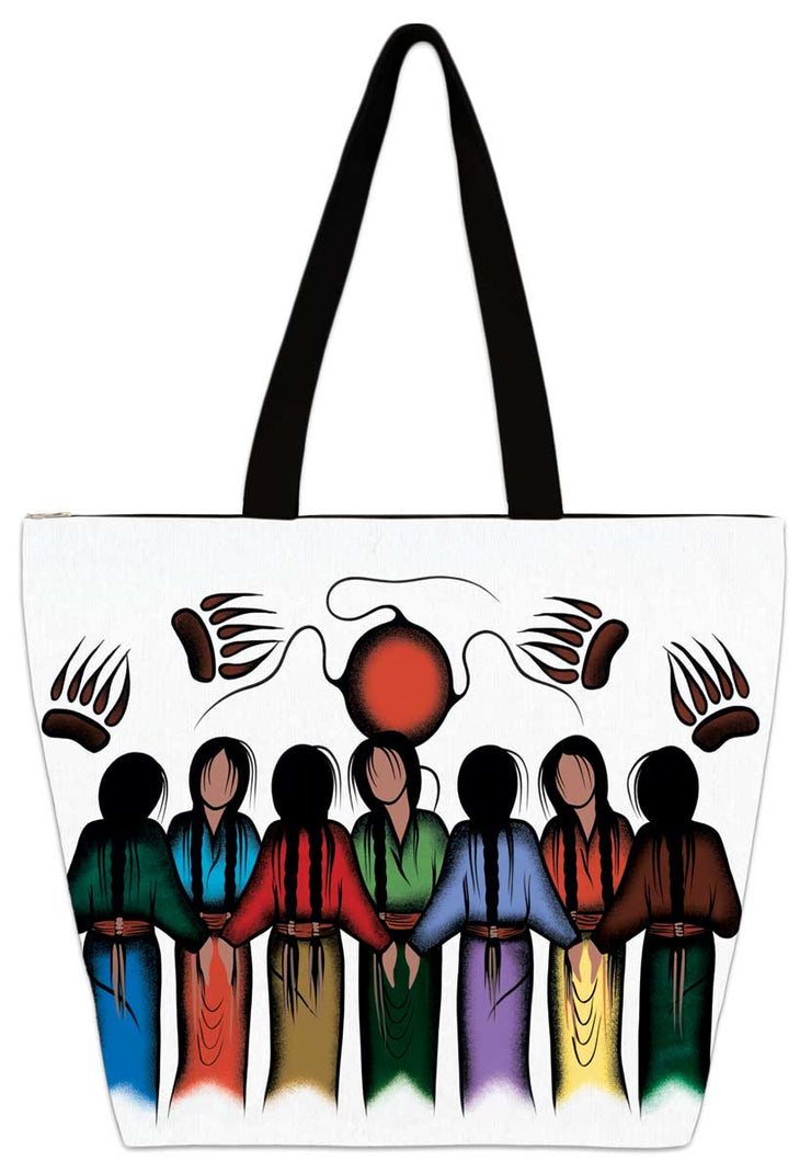 Seven women hold hands in a circle. Set under a red sun and four bear paw prints. Set on a tote bag.
