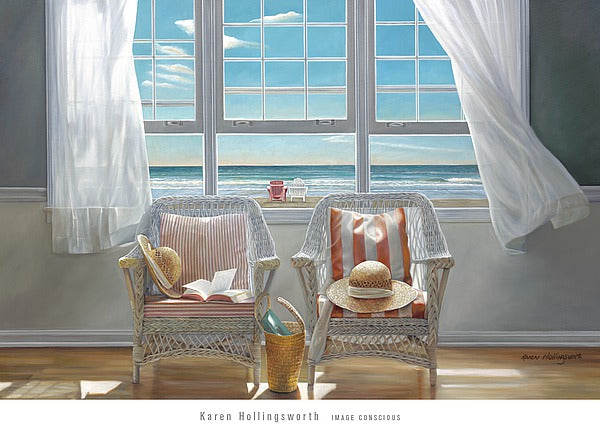 Two white, wicker chairs sit next to each other under an open window. Each chair has a white cushions with red stripes and a sunhat on them, one with an open book on it. A basket sits between the chairs. They sit on a wood floor with a grey and cream wall. The open window is split into three panes, with billowing, white curtains. A beach is seen outside the window, with a red and a white patio chair on the beach.