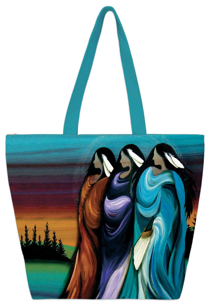 Three women stand against a sky painted by a setting/rising sun. They each wear two feathers in their long, dark hair. The left one wears a burnt orange, the center one purple, and the right one teal. Printed onto a tote bag.